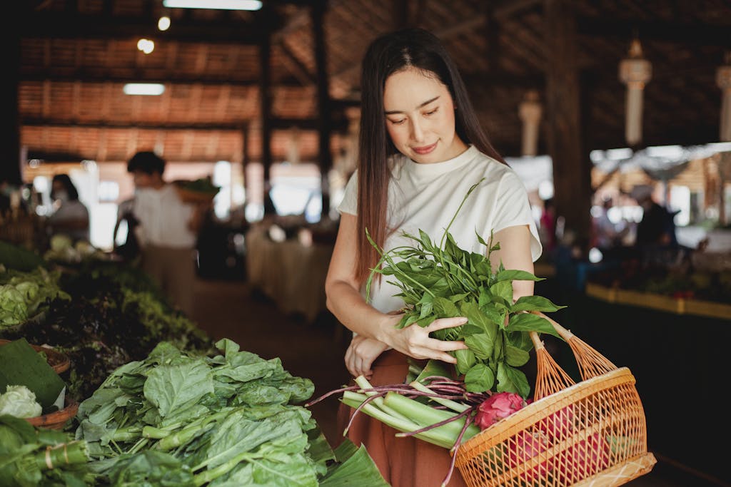 Young ethnic female putting aromatic fresh herb in wicker basket while looking down in local bazaar